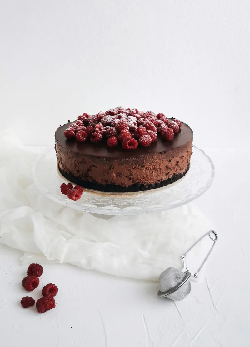 Chocolate cake topped with raspberries on a glass stand