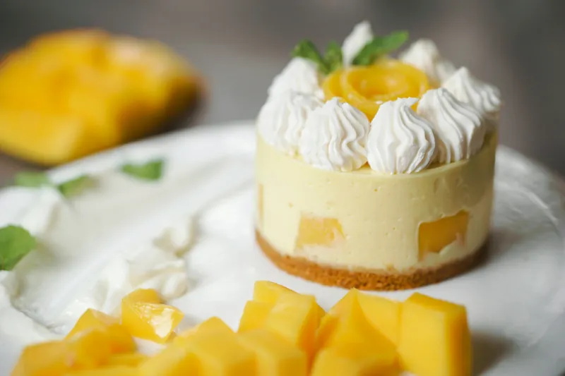 Mango cheesecake topped with cream swirls and fresh mango