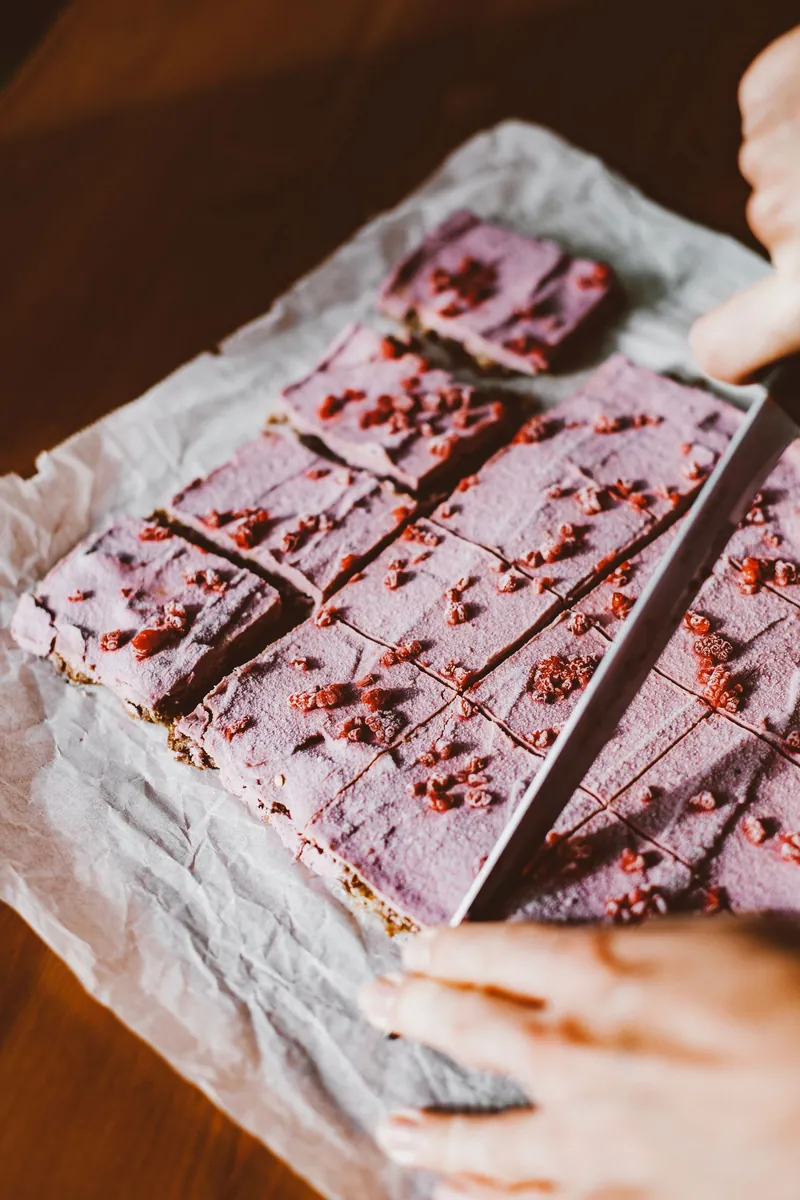 Hands cutting raspberry cream bars on parchment